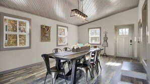 A spacious dining area with a long table and chairs, a ceiling light fixture, and artwork on the walls. - The Farmhouse Inn: 3 bed, 3.5 whole house rental (Hermann)