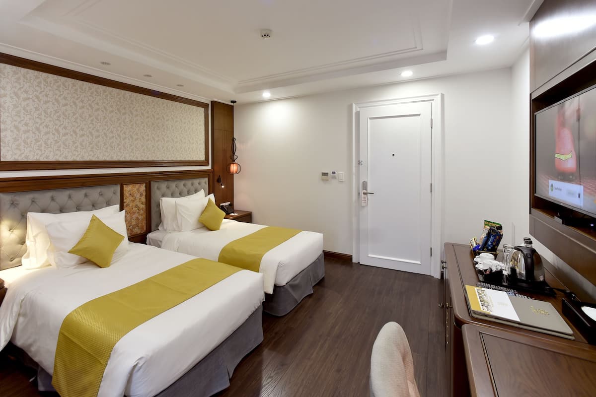 Ett hotellrum med två sängar, ett skrivbord, en TV och en dörr.