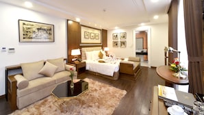 A well-lit hotel room with a bed, two sofas, a coffee table, and a small round table with a lamp and flowers. - Garco Dragon Hotel 2 (Hanoi)