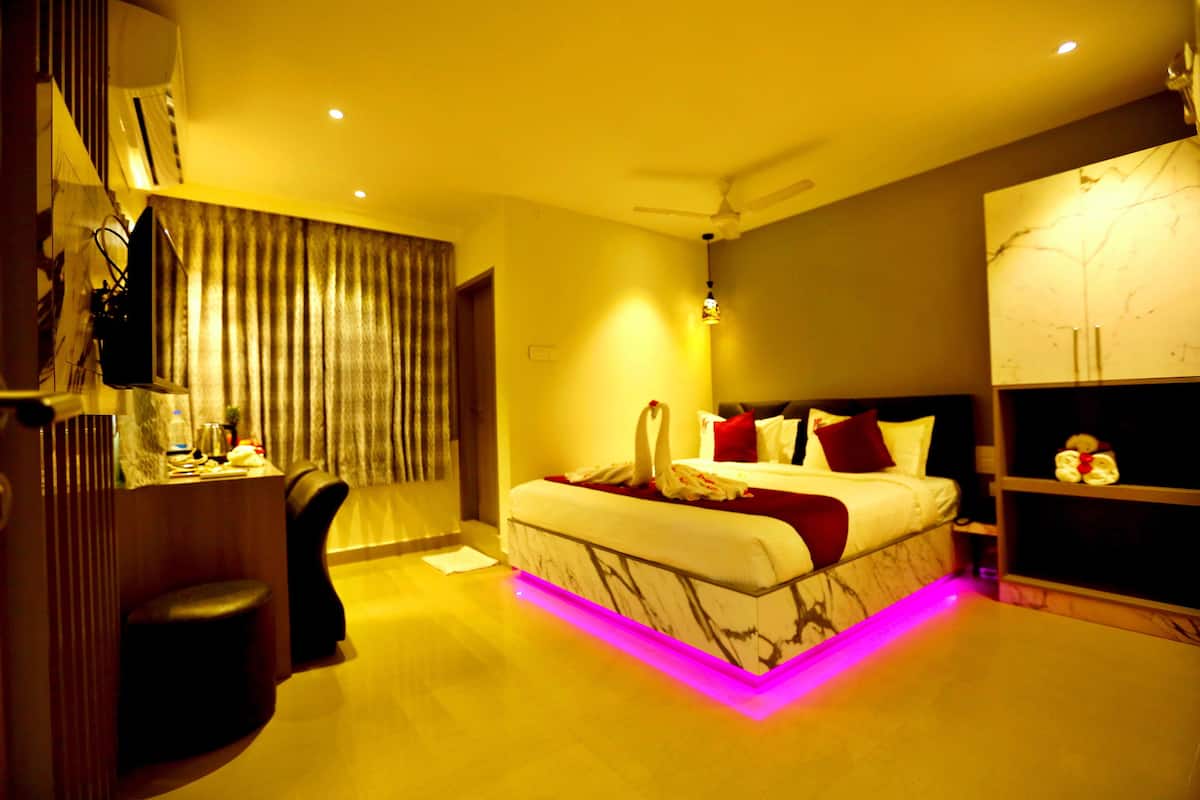 A modern hotel room with a marble headboard, a bed with red and white bedding, a desk with a chair, and a vanity with a mirror.