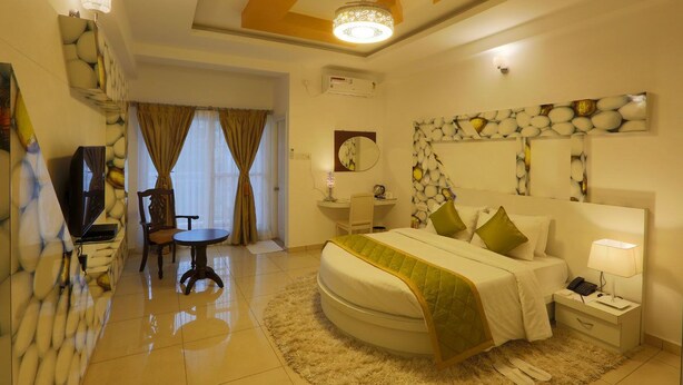 A hotel room with a bed, bedside table, lamp, chair, desk, and a TV. - High Sky Krishna Global Villaments (Bengaluru)
