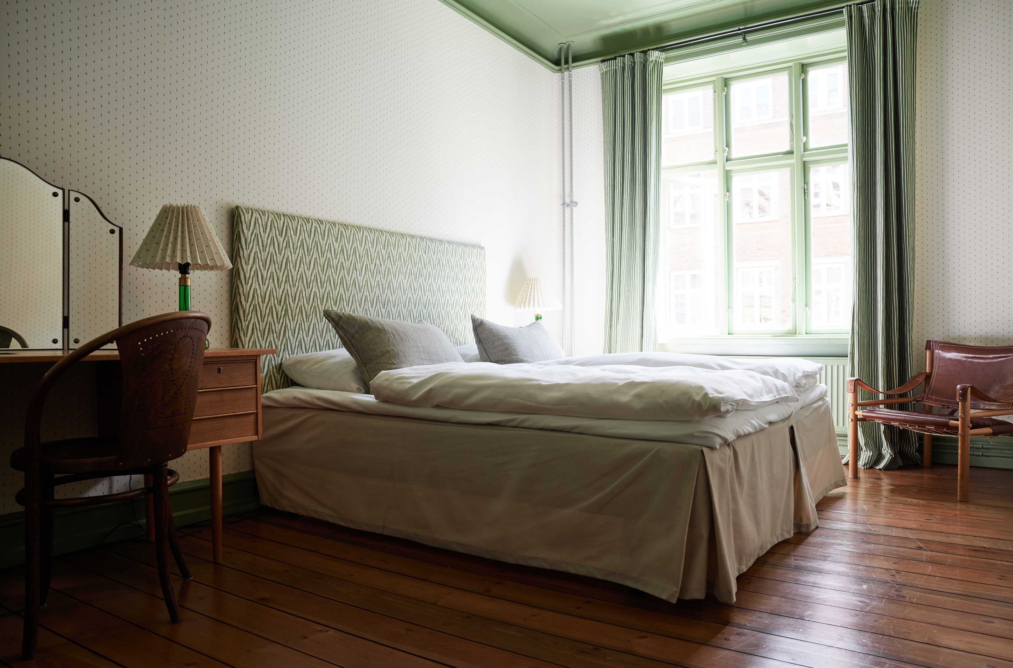 Une chambre à coucher avec un lit, un bureau, une chaise et une fenêtre avec des rideaux.