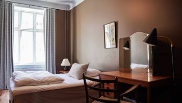 A hotel room with a bed, a desk, a chair, a lamp, a picture on the wall, and a window with curtains.