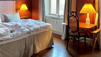 A hotel room with a bed, two bedside lamps, a chair, a table, and a window with curtains.
