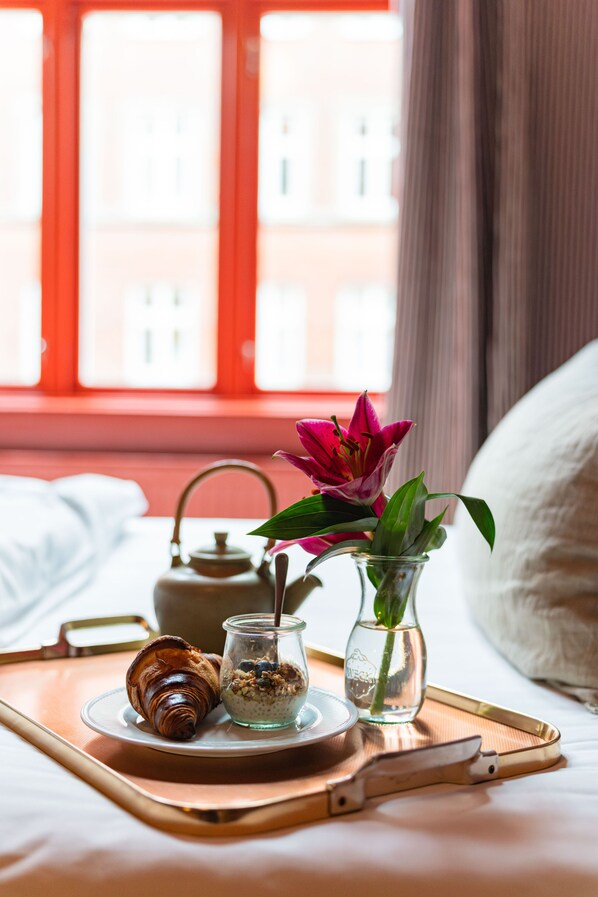 A breakfast tray with croissant, oatmeal, and a flower vase on a bed with a window view. - Rye 115 Hotel (Copenhagen)