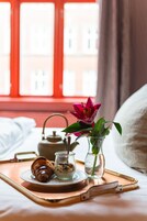 A breakfast tray with croissant, oatmeal, and a flower vase on a bed with a window view.