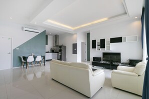 A modern living room with a sofa, a dining table with chairs, a kitchen area, and a TV. - CAPITAL O1009 Leleaf Valley Pool Villa Resort Hua Hin (Hua Hin)