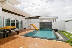 A modern outdoor swimming pool with a slide, wooden deck, and a small grassy area. - CAPITAL O1009 Leleaf Valley Pool Villa Resort Hua Hin (Hua Hin)