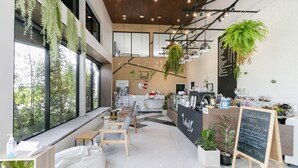 Um café moderno com amplas janelas, mobiliário de madeira e plantas penduradas.