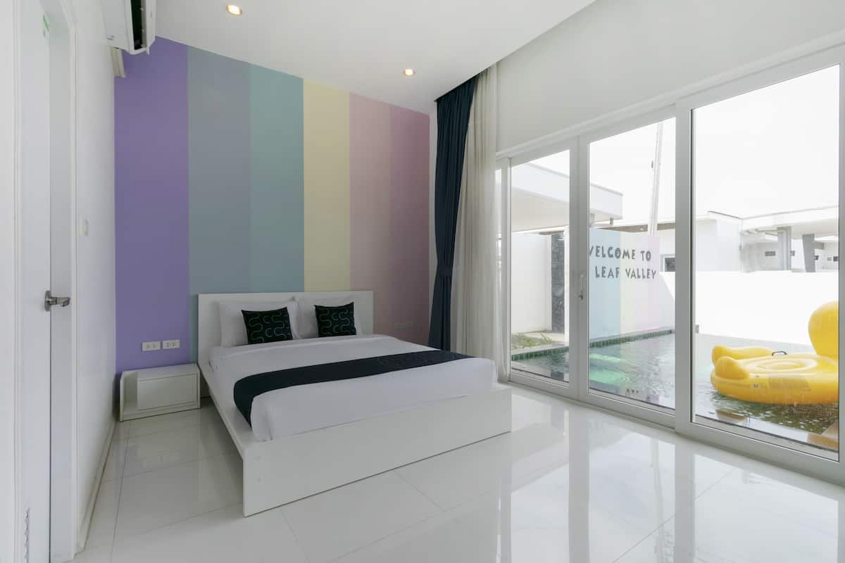 A modern bedroom with a large bed, a colorful wall, and a view of a pool area.