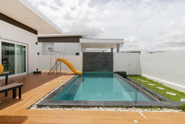 A modern outdoor pool area with a slide, wooden deck, and a stone wall. - CAPITAL O1009 Leleaf Valley Pool Villa Resort Hua Hin (Hua Hin)