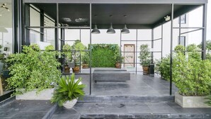 Entrada moderna de um edifício com um alpendre coberto, plantas em vasos e uma escadaria que leva à entrada.