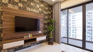 A modern living room with a large flat-screen TV mounted on a wooden wall with a geometric pattern. There is a potted plant and a small shelf with decorative items. - JAgape (Johor Bahru)