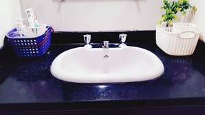 A bathroom sink with a white basin, two faucets, and a blue and white basket with toiletries. - Casa Sol de Maricá (Marica)
