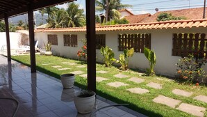A covered patio area with tiled flooring, potted plants, and a small garden with stepping stones. - Casa Sol de Maricá (Marica)