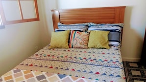 A bed with a patterned bedspread and multiple pillows, a wooden headboard, and a tiled floor. - Casa Sol de Maricá (Marica)