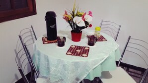 A round table with a lace tablecloth, a black electric kettle, a red mug, a yellow bottle, and a floral arrangement. - Casa Sol de Maricá (Marica)