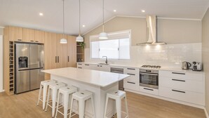 A modern kitchen with a central island, bar stools, a refrigerator, an oven, and a sink. - SEA BREEZE - Beachside Family Haven (Broadwater)