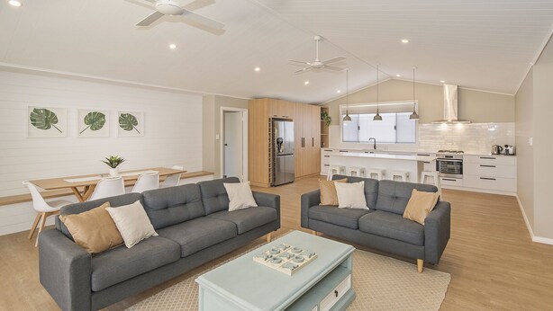 A modern living room with two grey sofas, a coffee table, and a kitchen in the background. - SEA BREEZE - Beachside Family Haven (Broadwater)