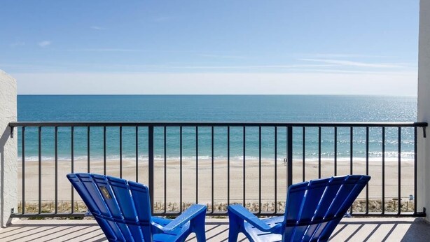 A balcony with two blue chairs overlooking a beach.