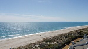 A beach view with a clear sky, sandy shore, and some buildings in the foreground.