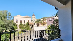 Varanda com vista para uma praça, uma igreja e vegetação ao redor.