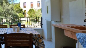 Uma cozinha com painel de azulejos, pia e janela com vista para um jardim e um edifício.