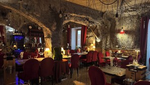 A restaurant with rustic stone walls, red velvet chairs, and hanging light bulbs. Tables are set with wine glasses and menus. - Auberge de la paix (Briançon)
