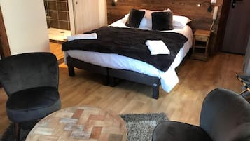 Una camera da letto moderna con un letto grande, due poltrone nere, un tavolino rotondo in legno e una testiera in legno.