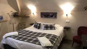 Een netjes opgemaakt bed met een geruit sprei en kussens, een rode stoel en een wandplank met een foto.
