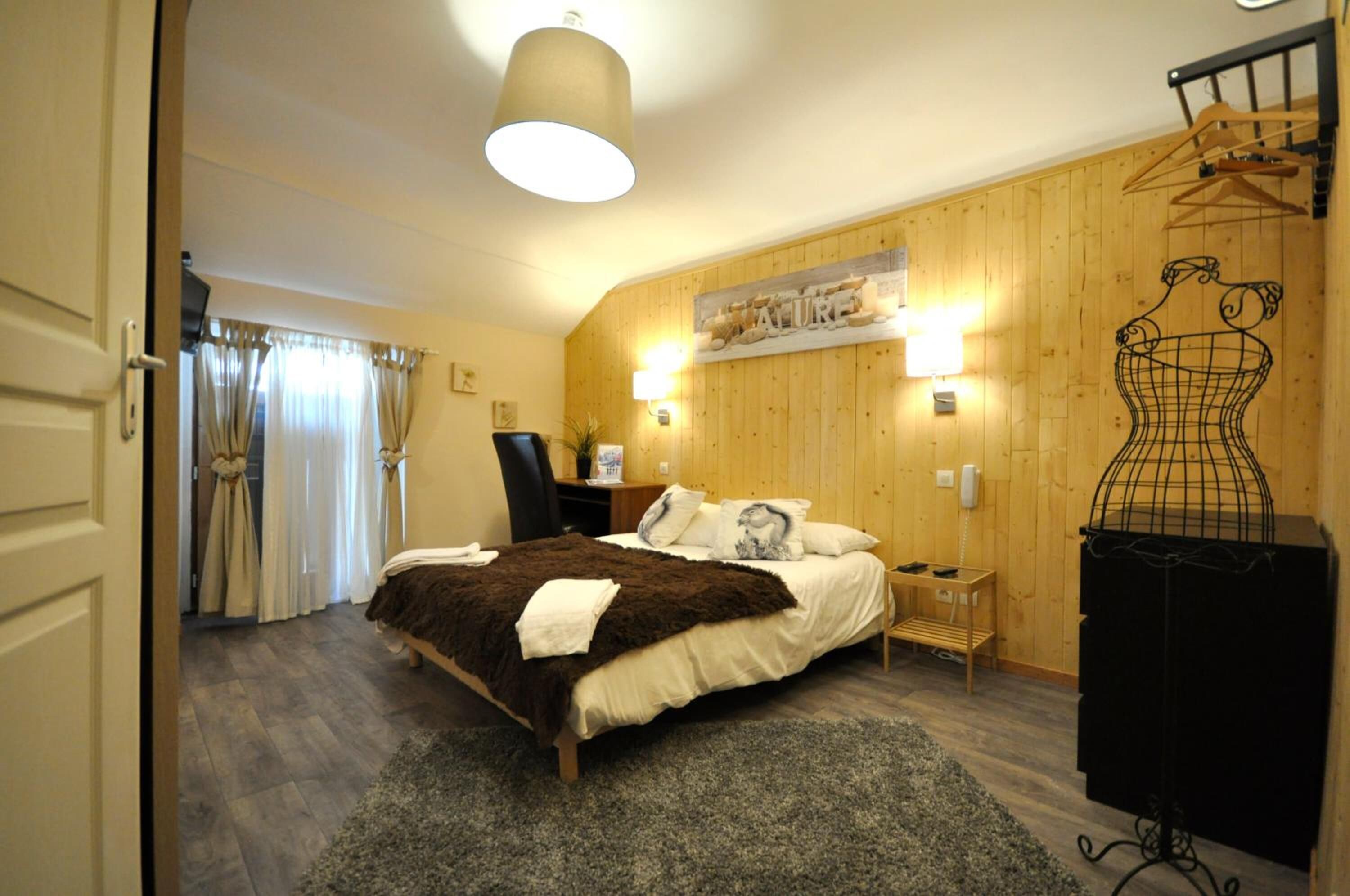 Een slaapkamer met een bed, een kapstok, een stoel, een lamp en een houten wand met een plank.