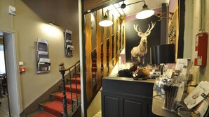 A staircase with red carpeted steps and a wooden railing, leading to a room with a black reception desk and a deer poster. - Auberge de la paix (Briançon)
