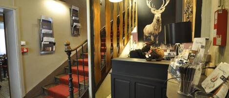 A staircase with red carpeted steps and a wooden railing, leading to a room with a black reception desk and a deer poster.