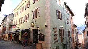 A narrow street with buildings featuring traditional architecture, including wooden shutters and a sign for a restaurant. - Auberge de la paix (Briançon)