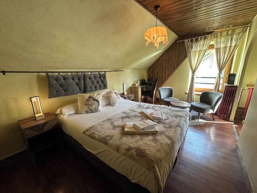 A bedroom with a large bed, a bedside table, a chair, a desk, and a hanging light fixture.