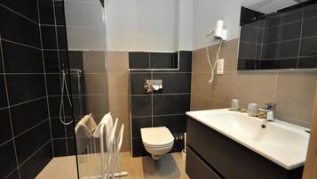 Un baño moderno con cabina de ducha de vidrio, un inodoro blanco y un lavamanos grande con espejo.