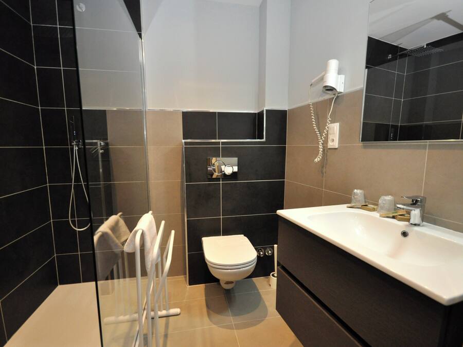 Un baño moderno con cabina de ducha de vidrio, un inodoro blanco y un lavamanos grande con espejo.