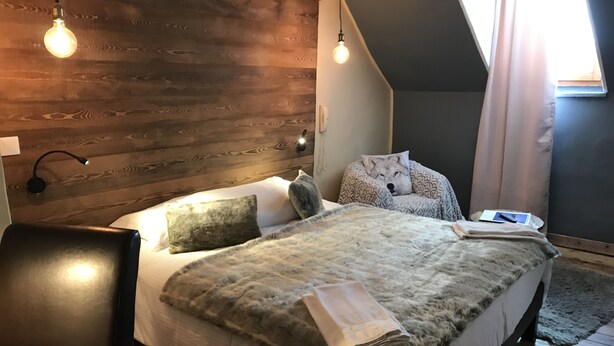 A modern bedroom with a wooden headboard, a large bed with a fluffy blanket, two bedside lamps, and a laptop on the nightstand. - Auberge de la paix (Briançon)