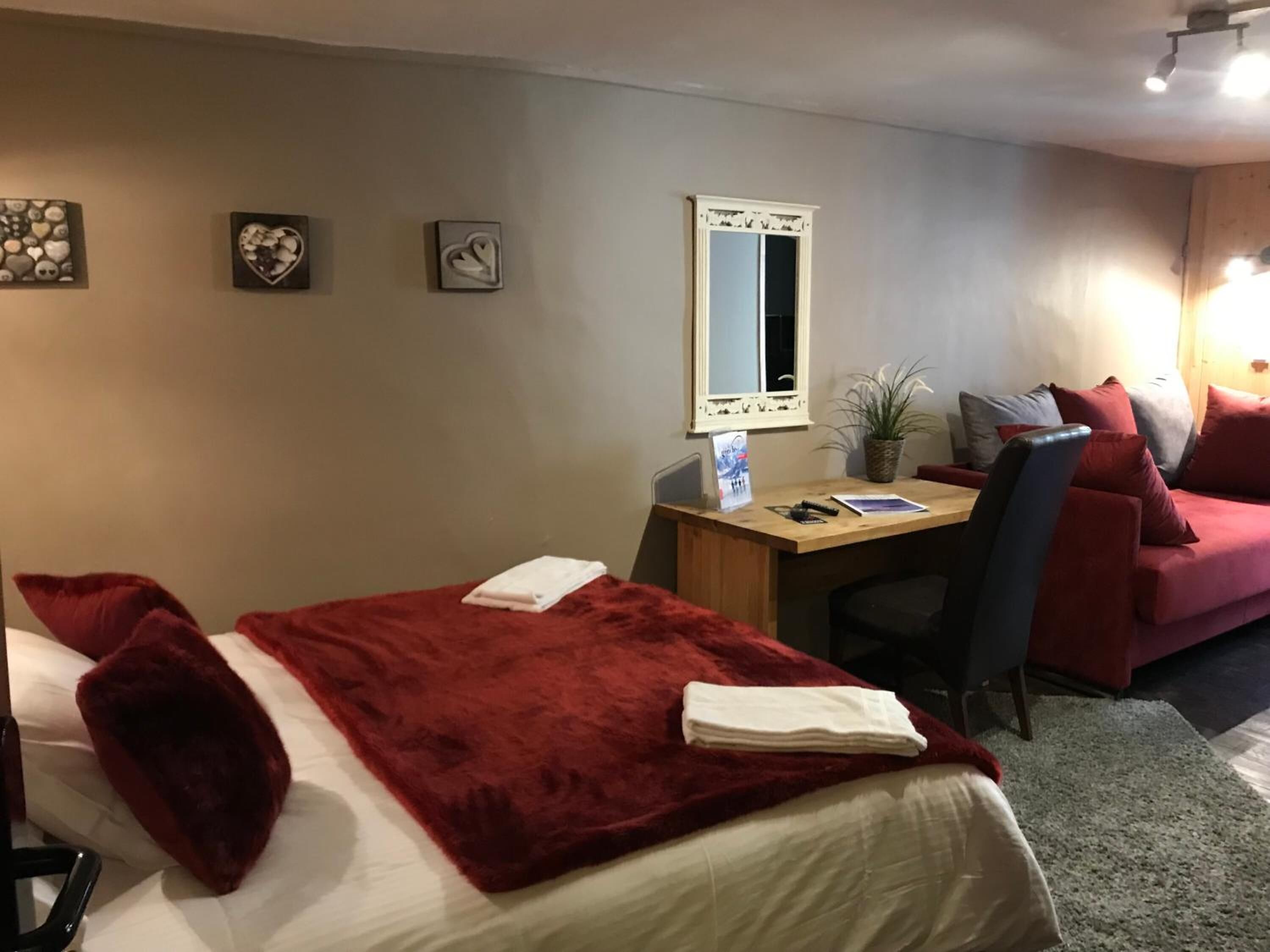 A hotel room with a bed, a desk, a chair, a red sofa, and a mirror on the wall.
