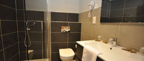A modern bathroom with a glass shower enclosure, a white toilet, and a large white sink with a towel.