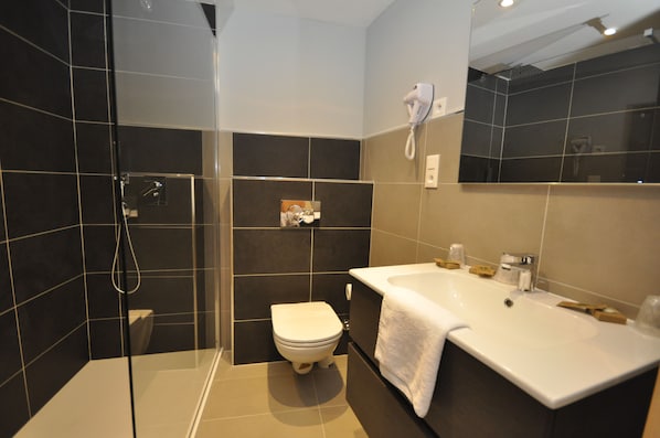 A modern bathroom with a glass shower enclosure, a white toilet, and a large white sink with a towel.