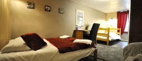 A bedroom with two beds, a desk, and a mirror.