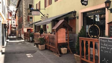 Una calle estrecha flanqueada por edificios, un restaurante con terraza y un letrero que indica restaurante.