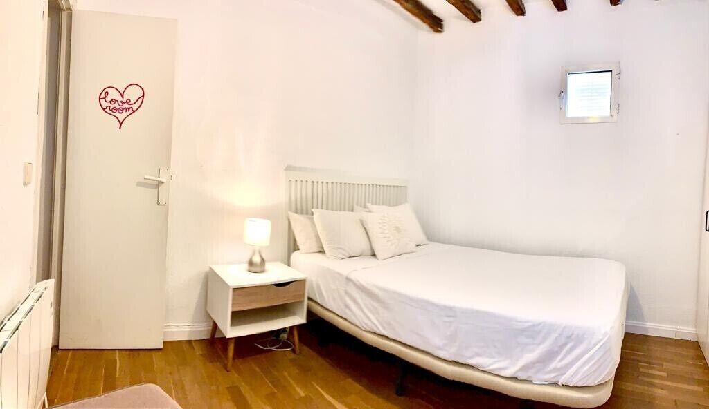 Un dormitorio con cama, mesita de noche, lámpara y una puerta con un símbolo de corazón.