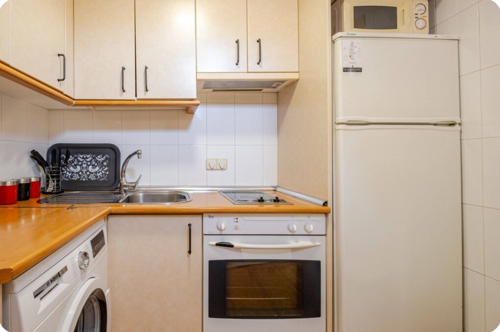 A compact kitchen with a washing machine, a microwave, and a refrigerator.