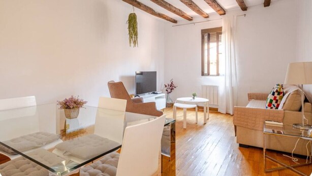 A modern living room with a glass dining table, white sofas, a TV, and wooden beams on the ceiling. - The apartment in Opera Royal Palace! (Madrid)