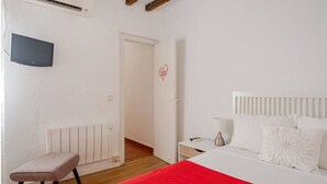A bedroom with a bed, a bedside table, a nightstand, a red blanket, a white radiator, a TV mounted on the wall, and a door leading to another room. - The apartment in Opera Royal Palace! (Madrid)