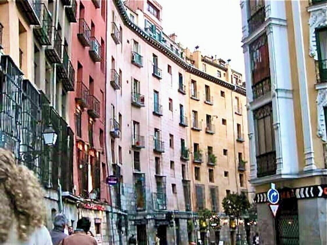A row of multi-story buildings with balconies, a street sign, and a pedestrian.
