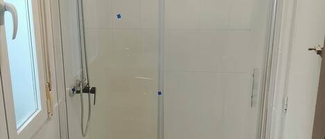 A glass-enclosed shower stall with a handheld showerhead and a wall-mounted faucet.