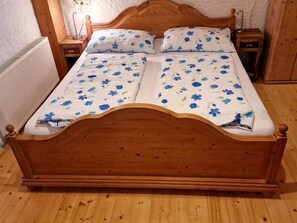 A wooden bed with a floral bedspread, two bedside tables, and a nightstand. - Family room - Pferde- und Schafhof Klinser (Vordertambergau)